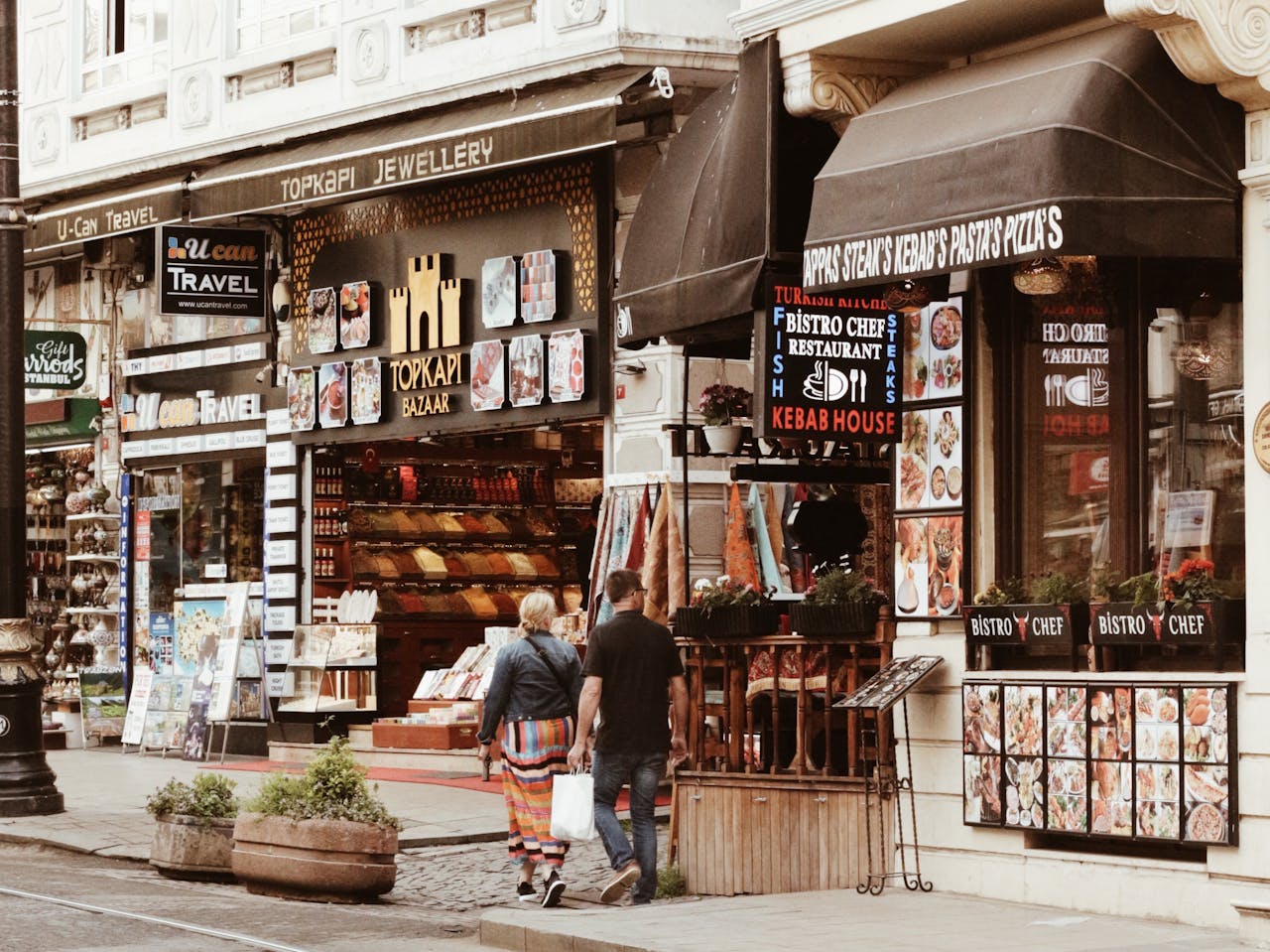 Couple walking through a lively city bazaar street lined with shops and eateries during the day.