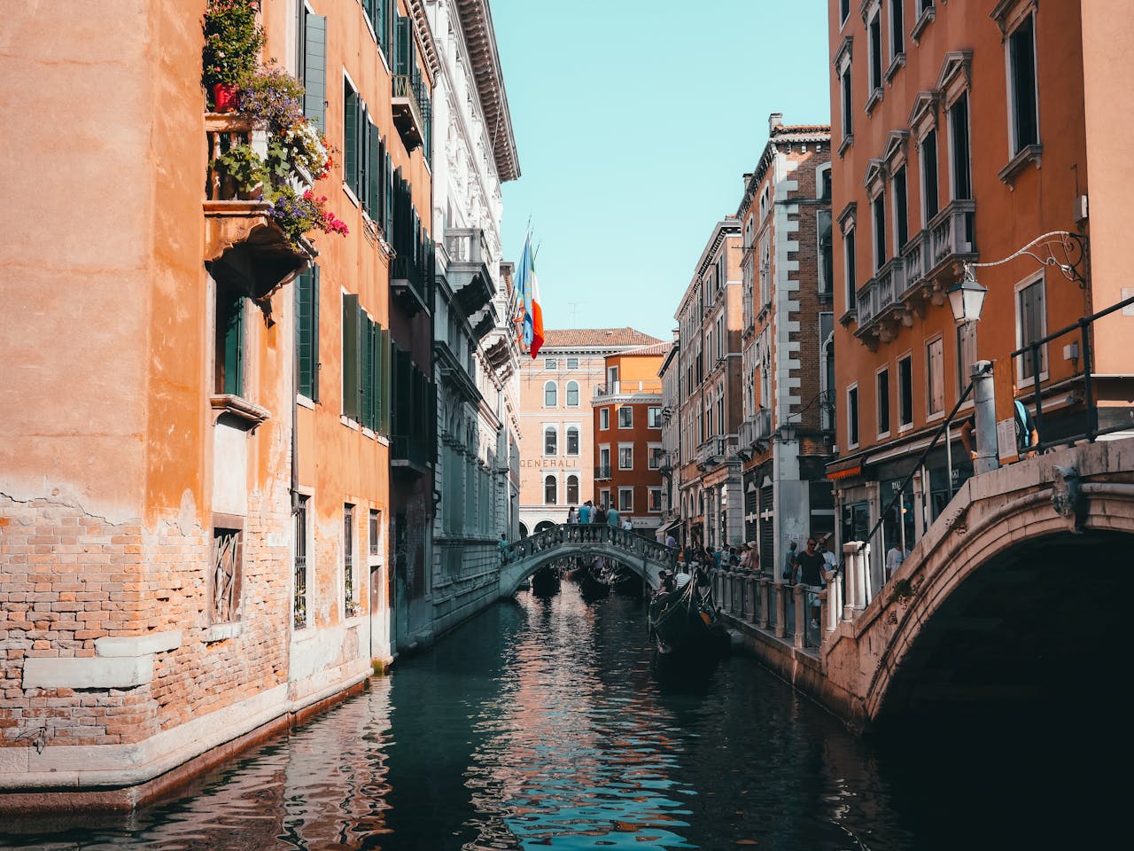 services-02 Beautiful view of a Venetian canal with classic architecture and a bridge under a sunny sky.