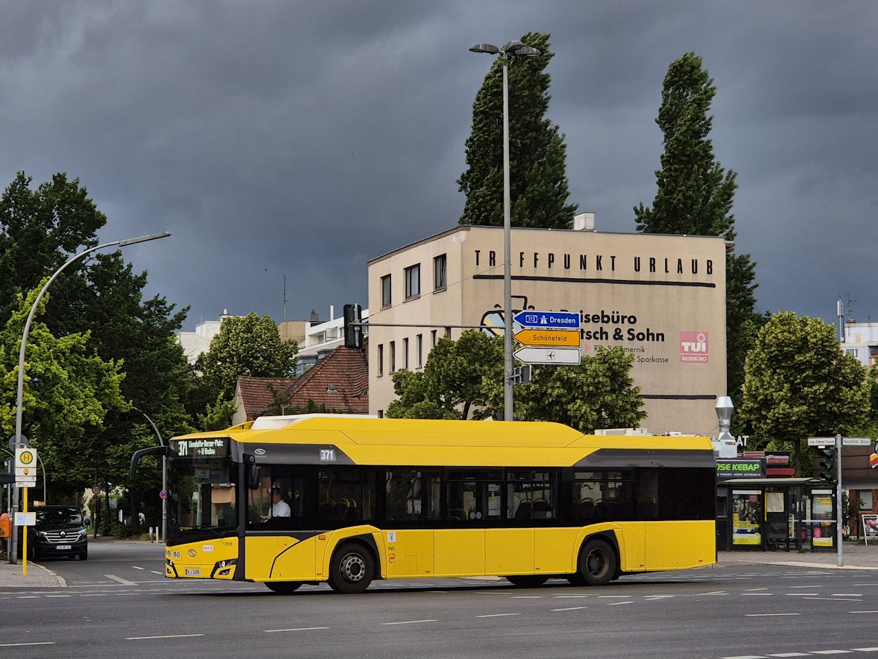 gallery-1 Yellow city bus crossing intersection in Berlin with stormy sky and travel agency background.