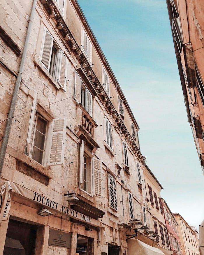 hero-img-02 Low-angle view of a rustic European street showcasing historic architecture and blue sky.